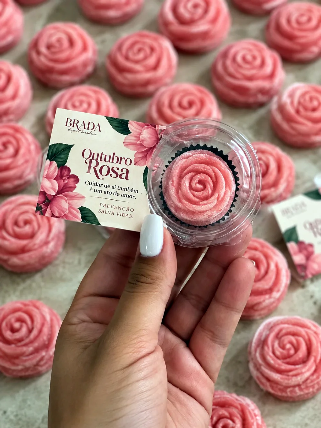 Brigadeiro em forma de flor com a tag de Outubro Rosa, na mão de quem entrega