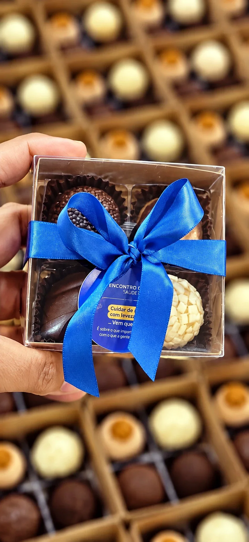 Caixinha com quatro brigadeiros, laço azul e a tag de um encontro, na mão