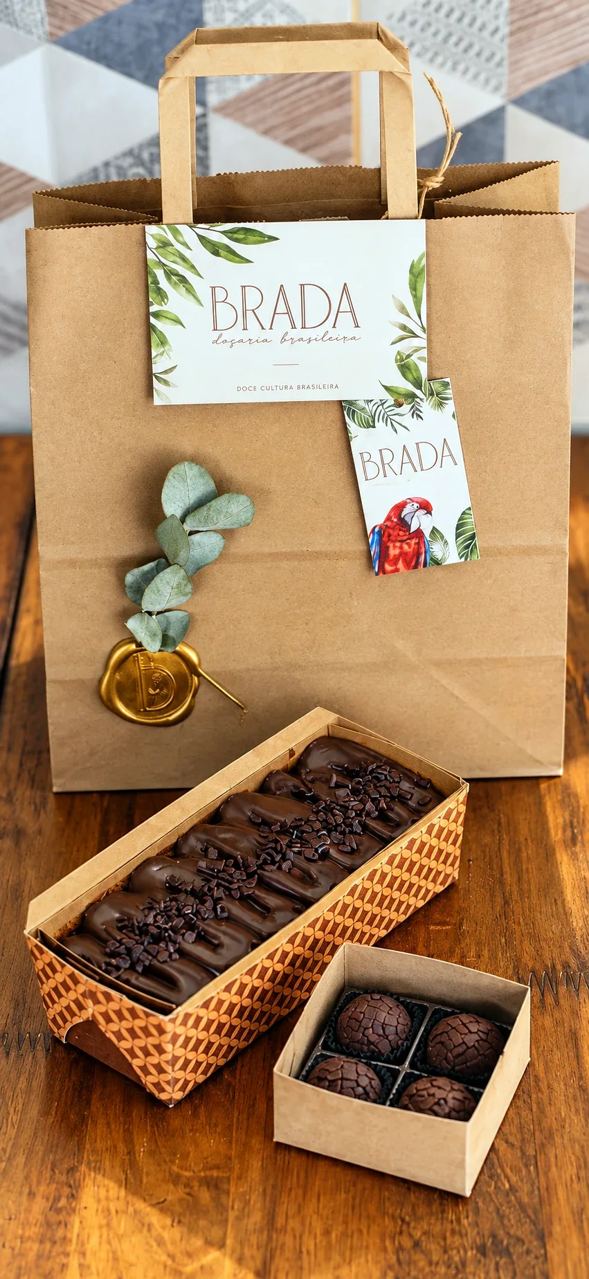 Sacola Mimo da Brada com tag e lacre, ao lado do bolo e da caixinha de brigadeiros