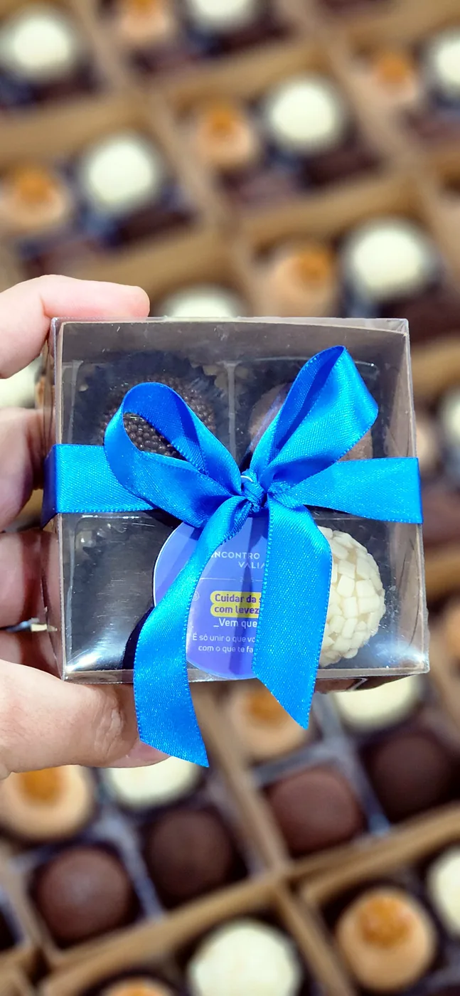 Caixinha com quatro brigadeiros, laço azul e a tag de uma empresa