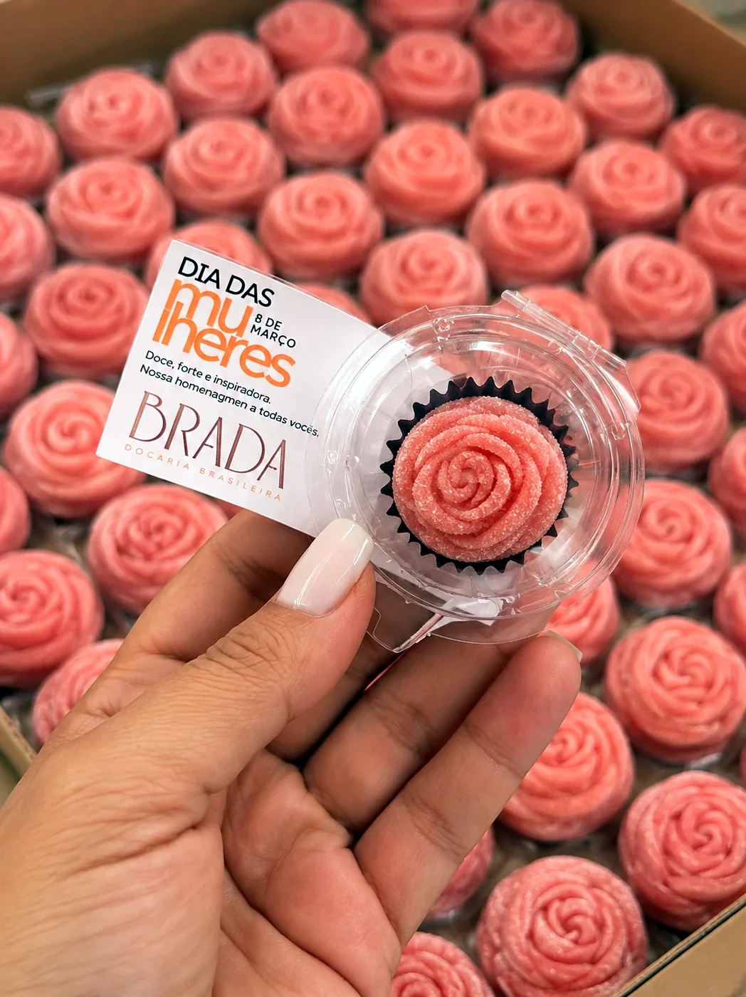 Doce unitário em forma de flor, com a tag de uma campanha, na mão